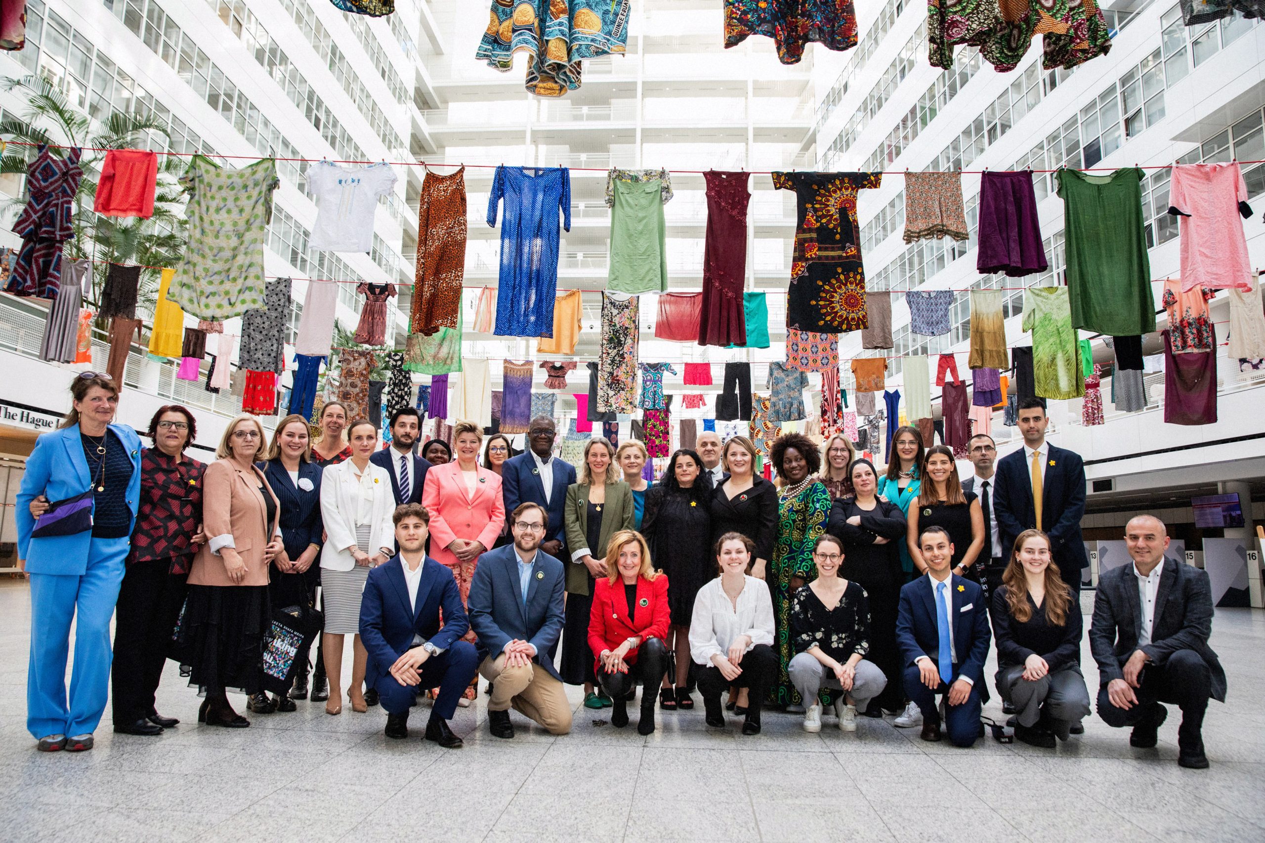 organisers and collaborators of Thinking of You posing under the dresses in the Atrium City Hall.