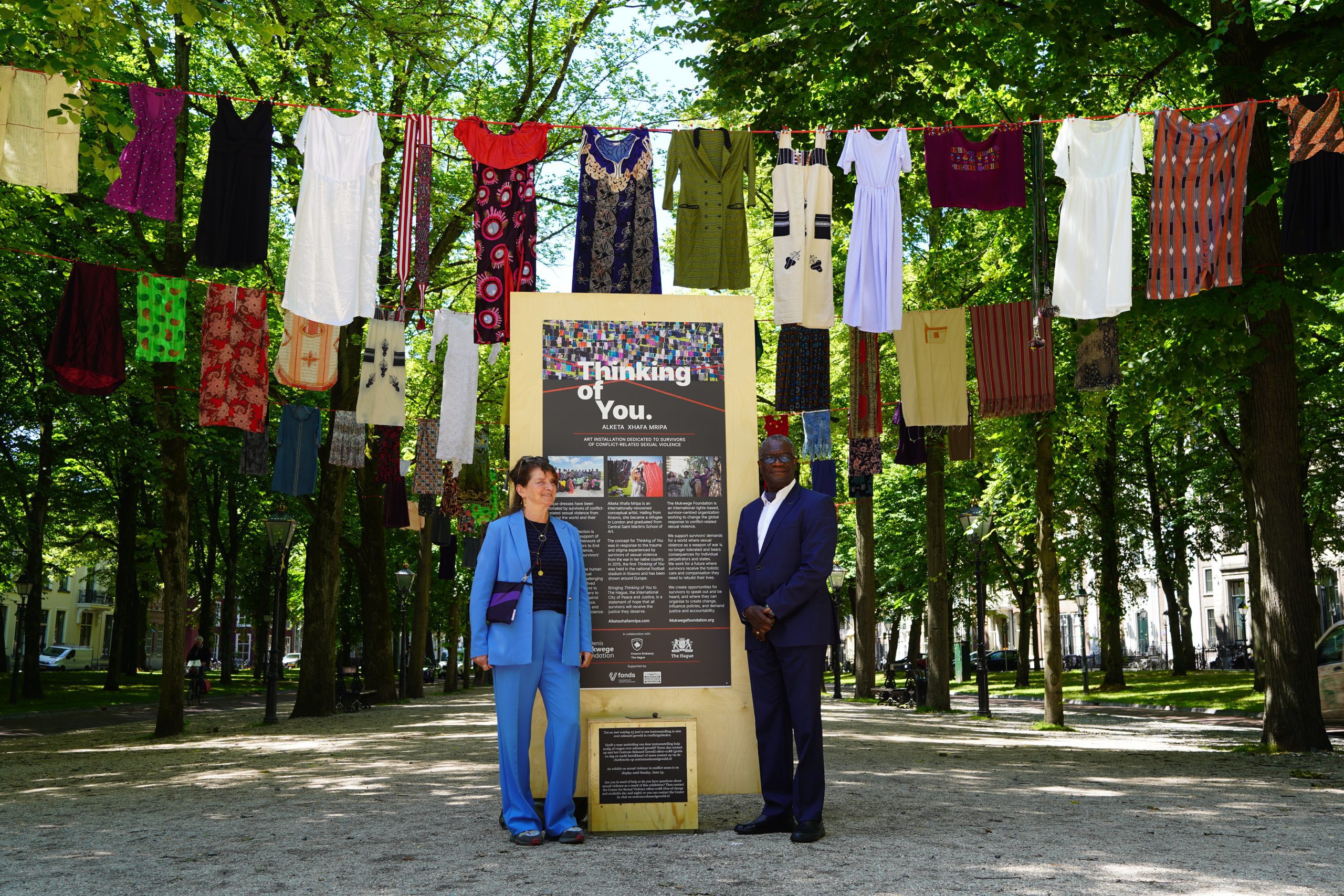 Katrien Coppens, director of the Mukwege Foundation, and Dr. Denis Mukwege, Nobel Peace Laurate 2018 leaning towards a sign in front of the outdoor exhibition Thinking of You (The Hague 2024) at Lange Voorhout.