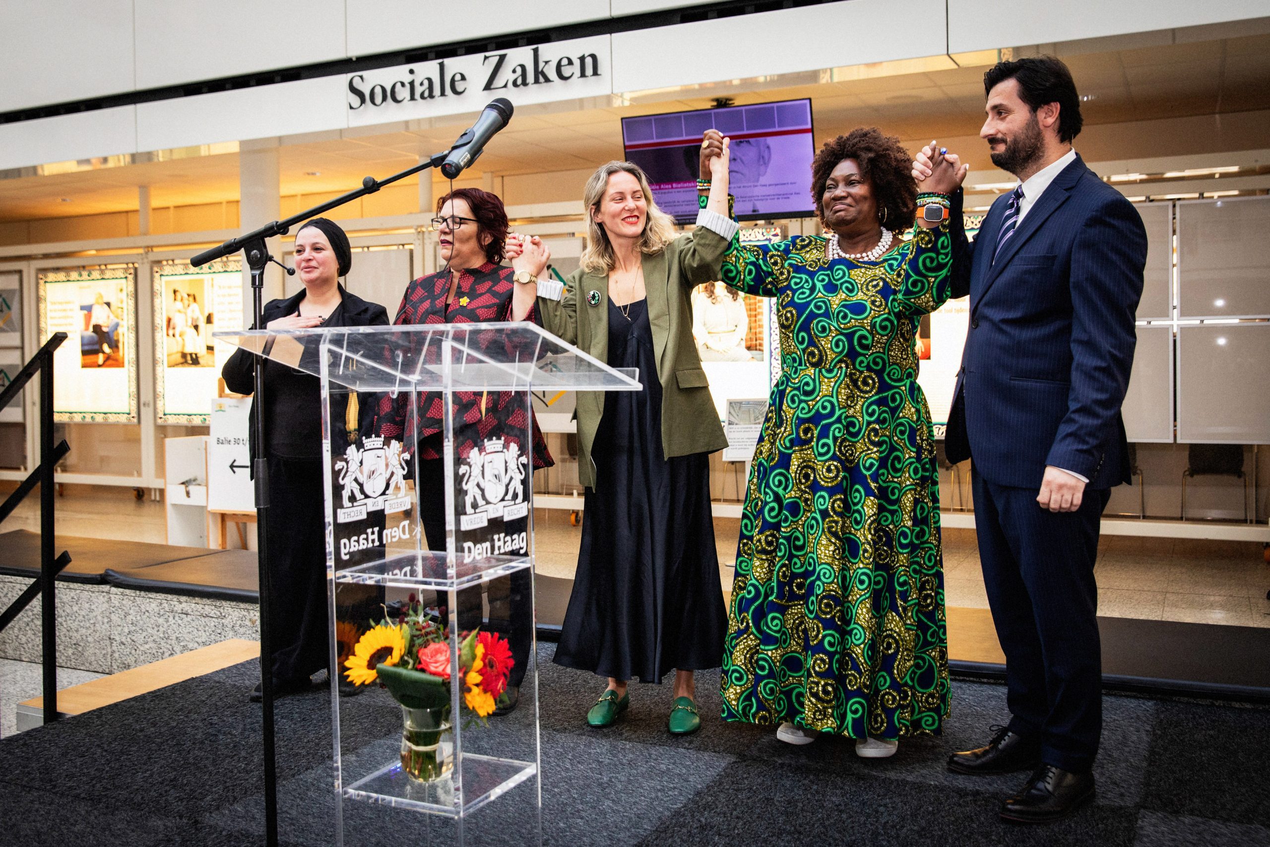 Survivors, the artist, and the Kosovo Ambassador standing on stage.